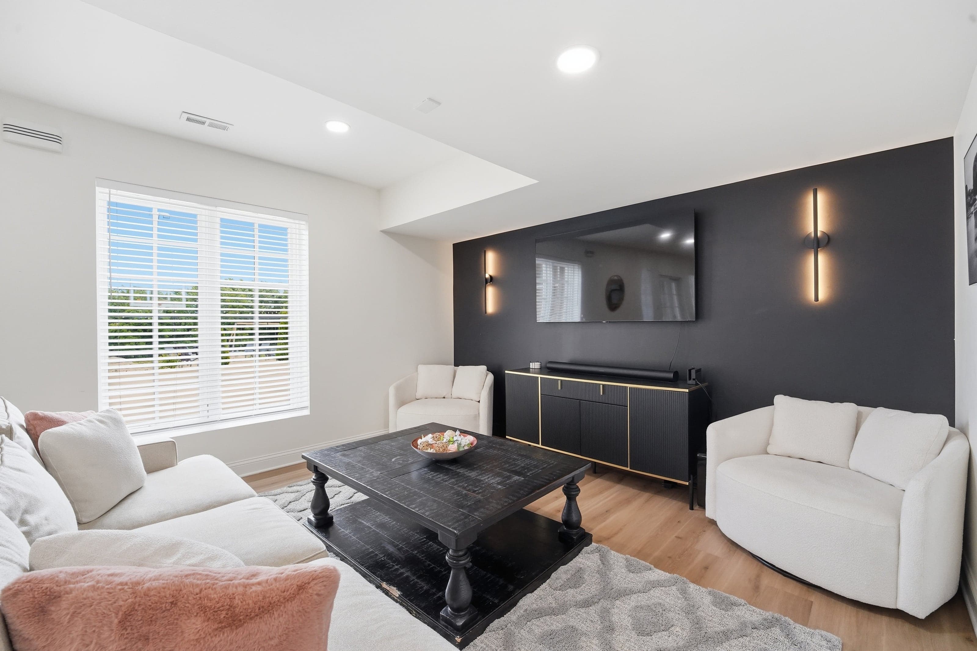 Living room with white sofas, a black accent wall and a mounted TV