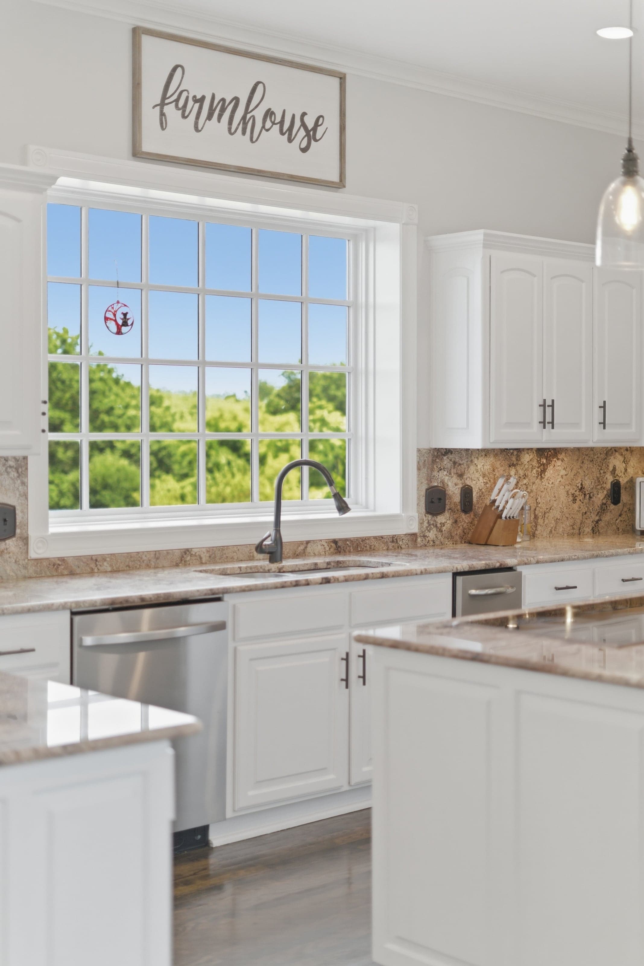 Kitchen window with a "farmhouse" sign above a granite backsplash and stainless dishwasher