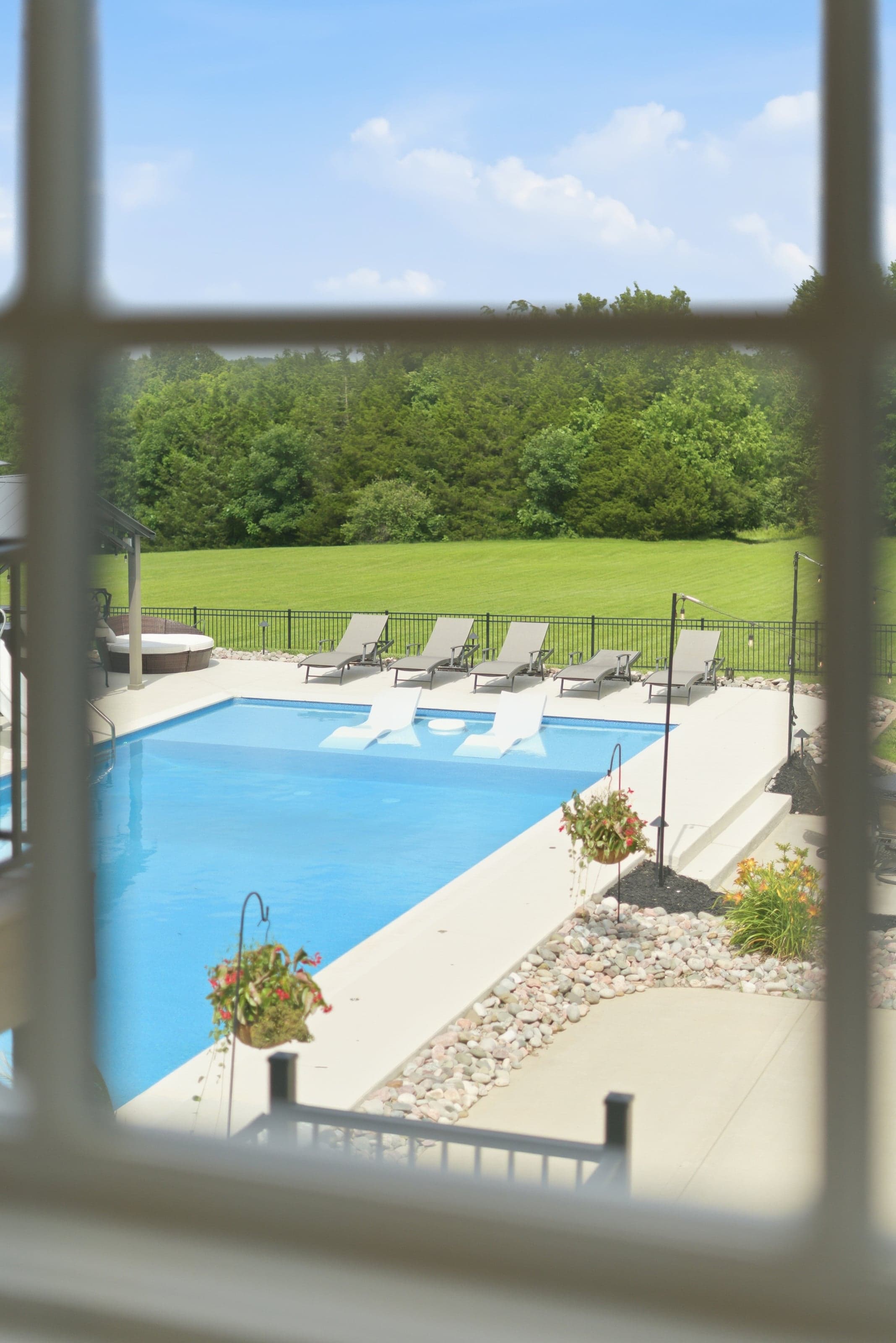 View through a window screen of a backyard pool with lounge chairs and a green lawn