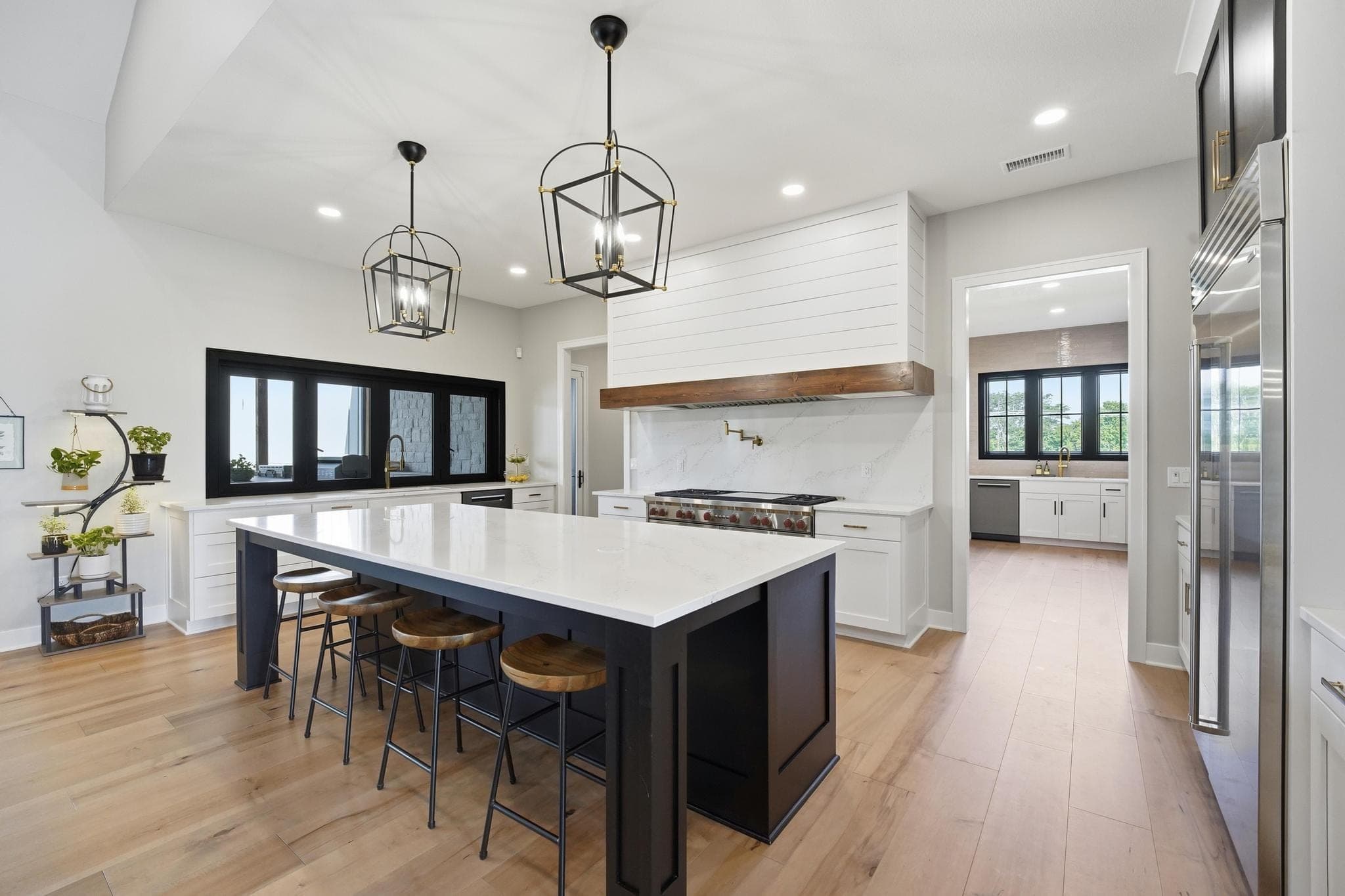 Kitchen with a black island, shiplap range hood and lantern pendants